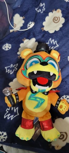 Customer's Glamrock Freddy plush holding a microphone while lying on a blue blanket.