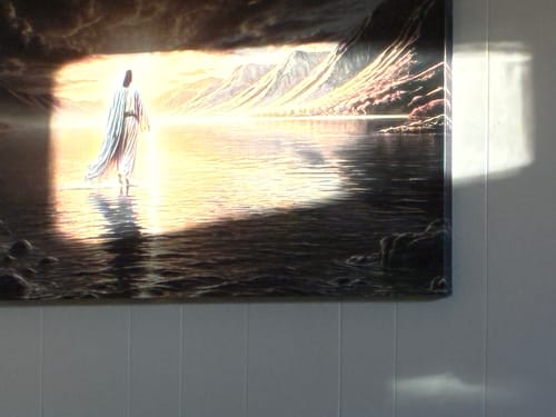 Customer's Walking on Water wall art hung on a white paneled wall, with a bright sunbeam shining across it.