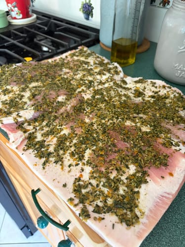 Customer's raw Duroc Pork Belly laid flat on a counter and seasoned with a thick layer of herbs before cooking.