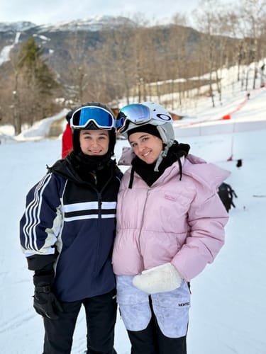 Customer in the navy retro sporty snow jacket with white stripes, standing on a snowy ski slope with another person.