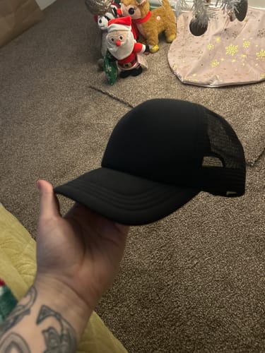 Reviewer holding a black Big Foam Trucker Hat, showing its mesh back and side profile.