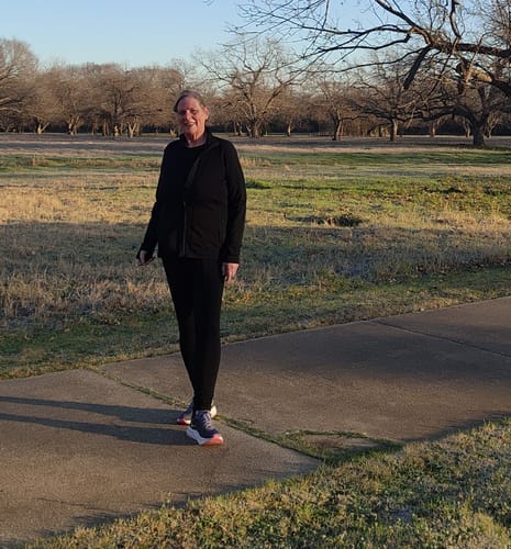 Reviewer standing on a path wearing the black Finley Zip Up Sweatshirt outdoors.