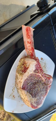 Customer's raw USDA Choice Tomahawk Ribeye, seasoned on a white plate before cooking.