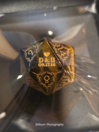Customer's close-up of the ornate Custom Anniversary D20 Dice personalized with initials and a date in gold lettering.