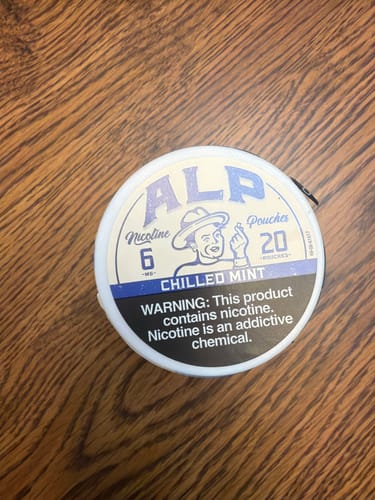Reviewer's can of ALP Chilled Mint nicotine pouches resting on a wooden surface.