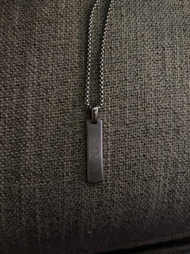 Customer's engraved Beveled Edge Bar Pendant on its box chain, shown on a dark textured surface.