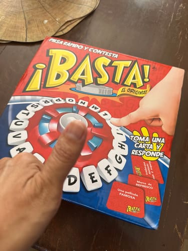 Un cliente muestra la caja del juego de mesa ¡Basta! con el pulgar hacia arriba en señal de aprobación.