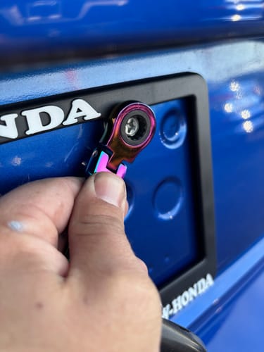 Reviewer using the iridescent 10mm Wrench Keychain to tighten a screw on a car's license plate.
