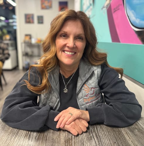 Reviewer smiling while seated, wearing a grey ThermoBall™ Trekker Vest with an embroidered logo over a black shirt.