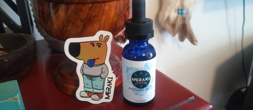 Customer's Meraki Blu Methylene Blue bottle and included sticker displayed on a red tabletop.