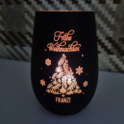 Kunde zeigt das personalisierte schwarze Windlicht. Es ist beleuchtet und zeigt die Gravur 'Frohe Weihnachten' und 'Franzi'.