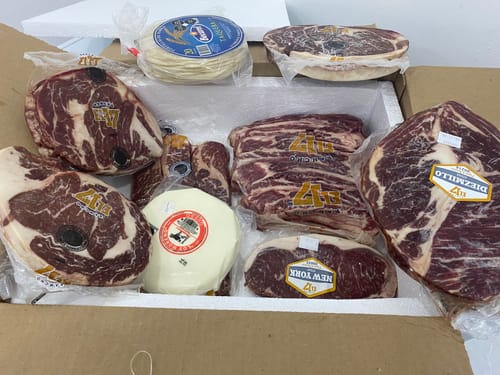El cliente muestra el Kit Carne Asada con varios cortes de carne, queso y tortillas envasados en una caja.