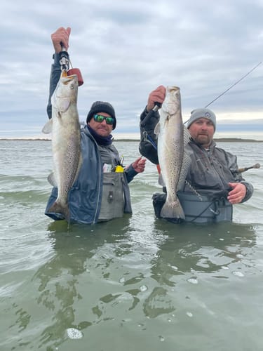 Two reviewers standing waist-deep in the water, each holding up a large speckled trout caught with Heddon One Knockers.