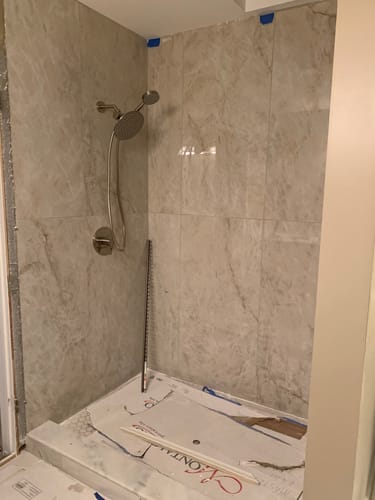 Reviewer's installed dual shower head system on a light, marble-patterned tile wall during a remodel.