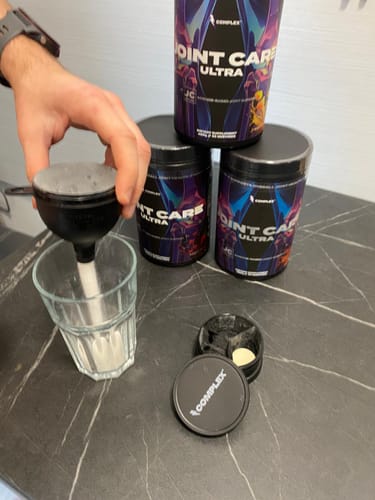 Reviewer using the black Complex Funnel to pour a supplement powder into a glass on a counter.