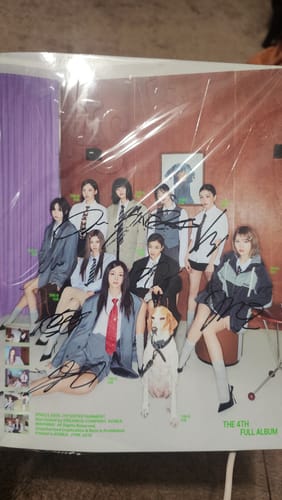 Reviewer's hand-autographed TWICE promo album, shown in its protective plastic packaging with signatures visible on the cover.