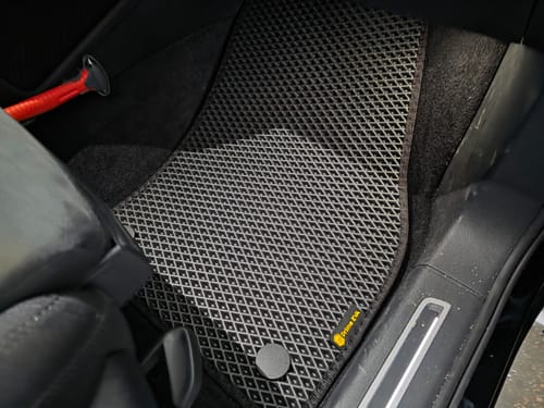 Recenzent pokazuje dopasowany, czarny dywanik samochodowy na podłodze po stronie pasażera.