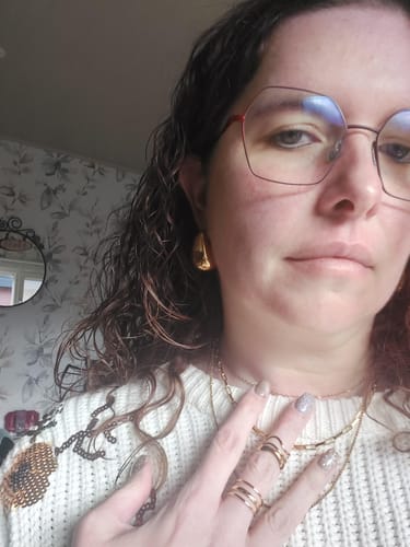 Customer showing four stunning gold jewelry pieces: a hoop earring, layered necklaces, and several rings.