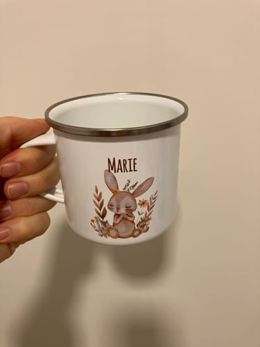Eine Kundin hält die personalisierte Emaille-Tasse mit einem Kaninchenmotiv und dem Namen 'Marie'.