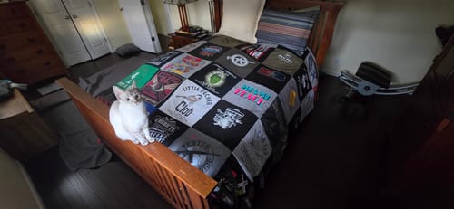 Customer's large T-Shirt Quilt spread on a bed in a bedroom, with a cat sitting on the footboard.