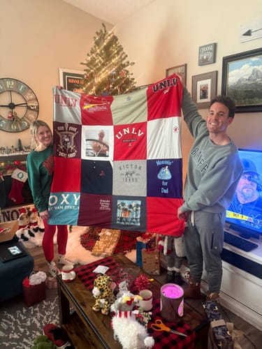 Customer and another person holding up their finished Premium T Shirt Quilt in a festive living room.