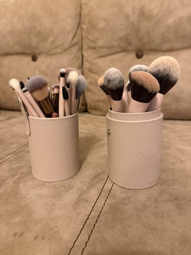 Customer's makeup brush set in its two-part, light pink cylindrical holder, displayed on a tufted couch.