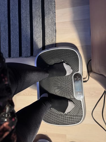 En anmelder står på sin vibrationstræner set fra oven på et trægulv.