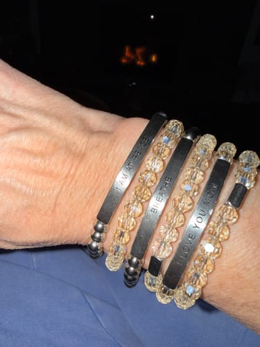 Reviewer's wrist showing a stack of beaded BREATHE bracelets with different inspirational engravings.