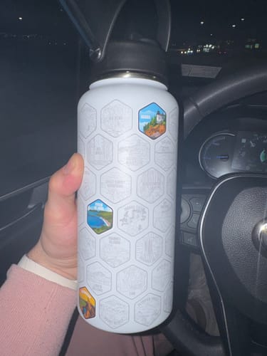 Reviewer holding their white National Parks Water Bottle in a car, with three colorful park stickers applied.