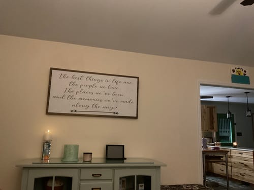 Customer's framed 'The Best Things In Life Sign II' hanging on a wall above a credenza in a living room.