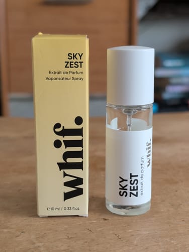 Customer's Sky Zest perfume bottle and its pale yellow box standing on a wooden surface.