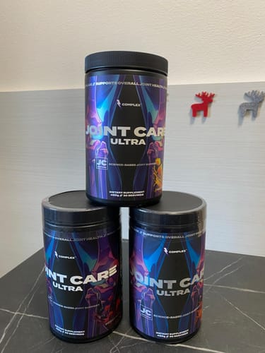 Reviewer's three black tubs of Complex Joint Care Ultra stacked in a pyramid on a dark countertop.