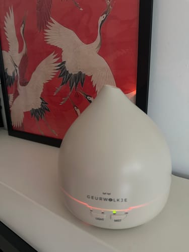 Klant toont de ingeschakelde warmgrijze Unity 2.0 Aroma Diffuser op een dressoir.