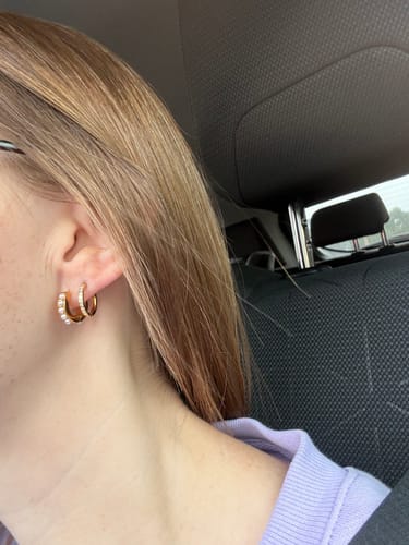 Close-up of a reviewer's ear, showing two small gold Eternity Hoop Earrings hugging the lobe.