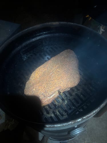 Reviewer's seasoned USDA Prime Brisket smoking inside a large, round grill at night.