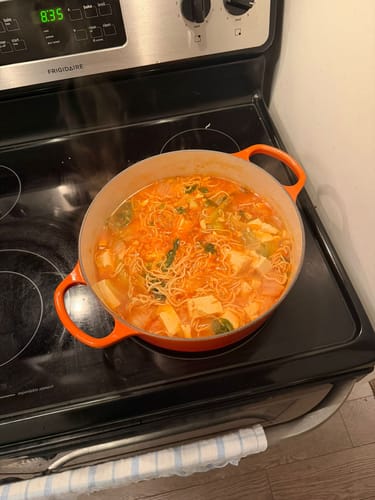 Customer's orange Le Creuset French Oven on a stovetop, filled with a steaming hot stew.
