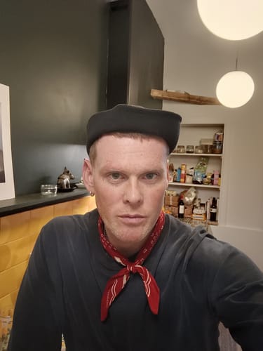 Customer wearing the navy WWII US Navy Dixie Cup Hat, looking directly at the camera in a home setting.