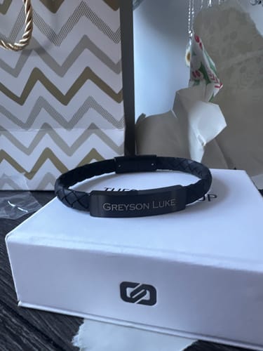 Reviewer's engraved black leather ID bracelet resting on top of its white product box.