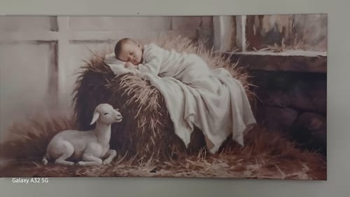 Customer's Peaceful Nativity Christmas Wall Art hanging on a wall, showing baby Jesus sleeping on hay with a lamb nearby.