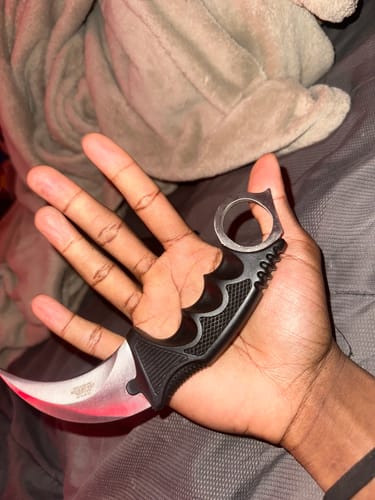 A customer holds the Raptor Karambit knife in their palm, showing the black, ergonomic grip and curved silver blade.