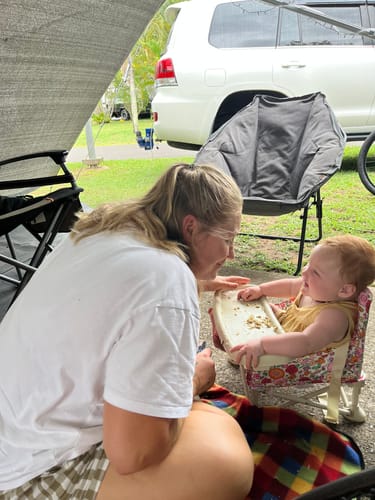 Customer's baby eating from the tray of a floral Paloma baby chair v2 while at a campsite.