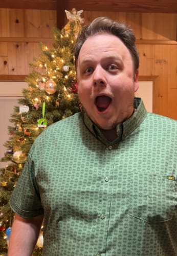 Reviewer with an excited expression wearing the green Muppets 'Goin' Green' shirt in front of a Christmas tree.