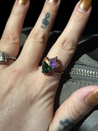 Close-up of a reviewer's hand wearing the Navae Birthstone Ring with a vibrant green pear-cut and pink radiant-cut stone.