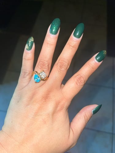 Customer's hand wearing the Navae Birthstone Ring with a blue pear-cut stone and a clear radiant-cut stone.