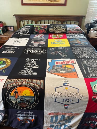 Customer's colorful Premium T Shirt Quilt with various logos spread neatly across a bed, viewed from the foot of the bed.