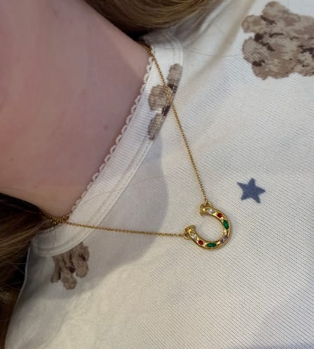 Close-up of a reviewer wearing the Lady Luck Horseshoe necklace, showing the pendant with colorful gems.