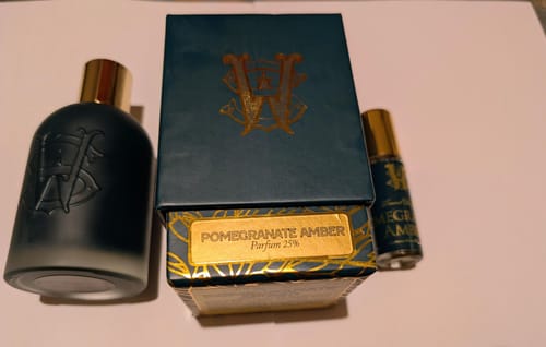 Reviewer's Pomegranate Amber perfume bottle, dark box, and travel-size rollerball displayed together.
