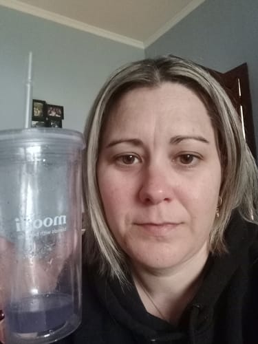 Reviewer holding a clear cup with the purple Blackcurrant Apple drink inside.