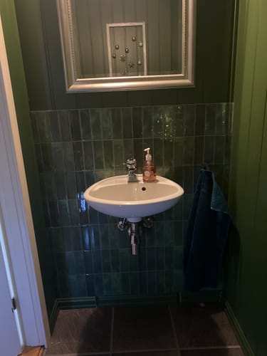 Kundens Adelina grønne selvklebende veggfliser installert på en baderomsvegg bak en liten vask.