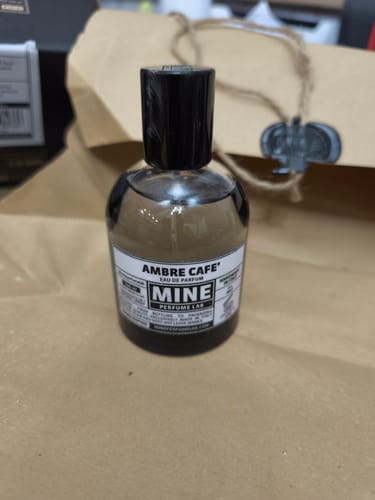 Recensore mostra il flacone di profumo AMBRE CAFE' davanti alla sua confezione di carta.